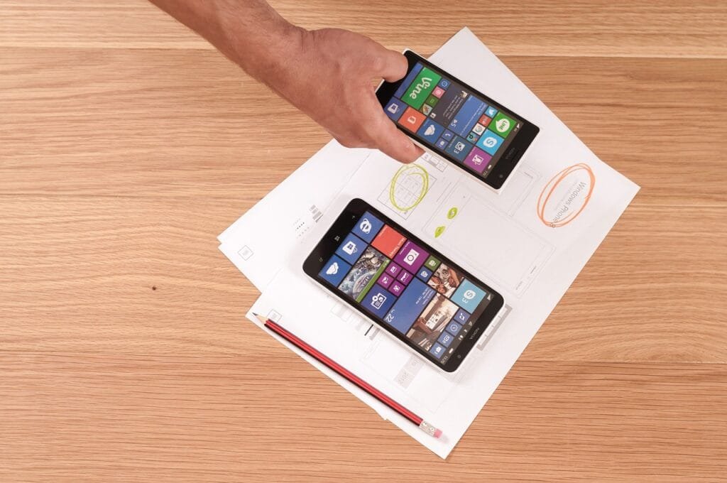 A person is holding a smartphone and a tablet, both placed on a table, showcasing modern technology usage.